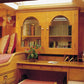 A warm wood-paneled interior room with built-in bookshelves, two beds with red patterned bedding, a desk, and ceiling fans.